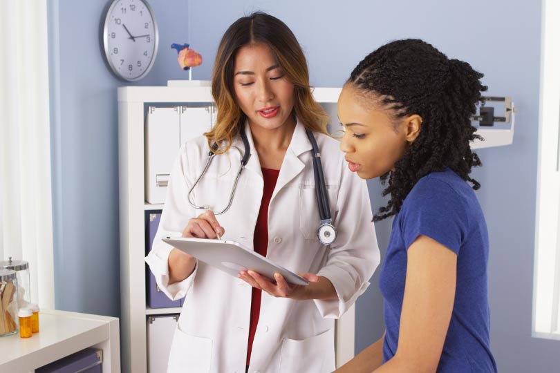 A female patient sits in a doctor’s office with a female healthcare provider, discussing colorectal cancer screening.