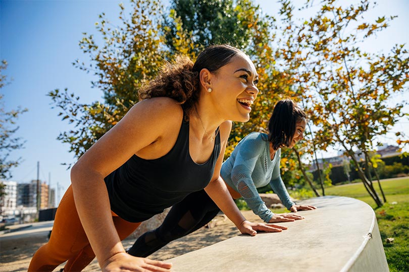 Two young women working out outside, laughing and smiling together, talking about the benefits of hormone testing in women’s health. 