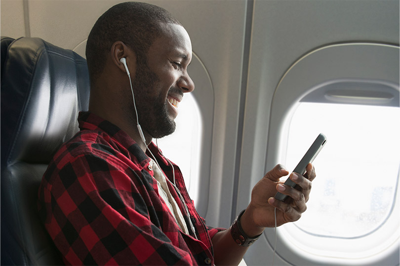 A man sitting on an airplane listening to music and reading on his phone about blood tests that offer health insights beyond an annual physical exam. 