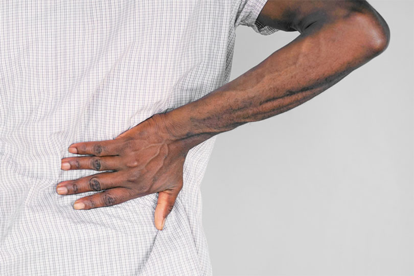 The back of a Black man placing his hand on his waist near his kidneys 