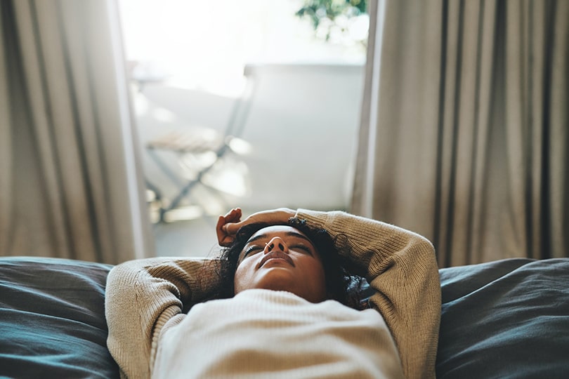 Woman lying on a bed with her eyes closed, thinking about fatigue and whether she may have a vitamin B12 deficiency. 