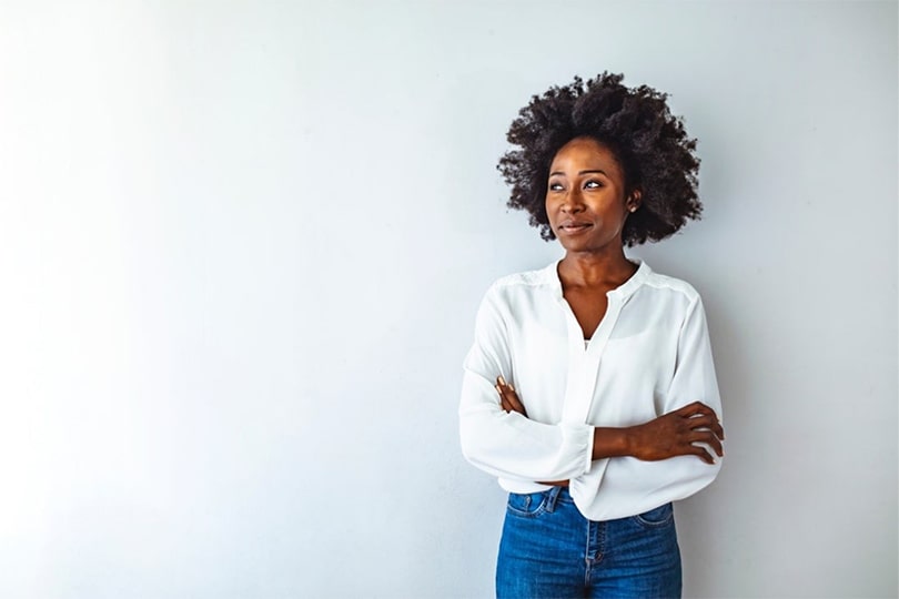 A woman standing with her arms crossed looking to the side, thinking about the difference between GlycA and hs-CRP inflammation markers for heart health.