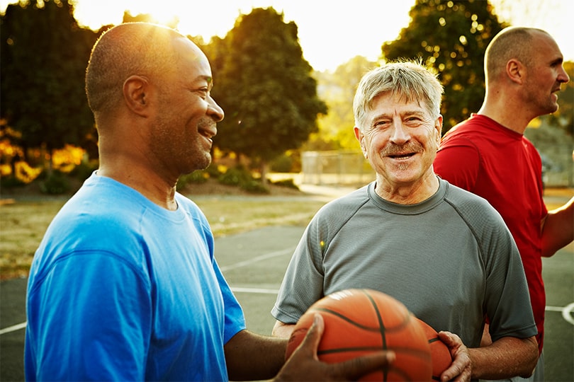 Three older men outside playing basketball, talking about male hormone health.