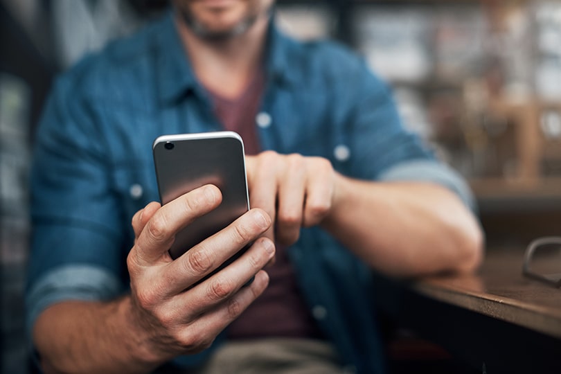 An adult man sitting at a table looking at his phone, researching how soon after unprotected sex one should get tested for STIs.