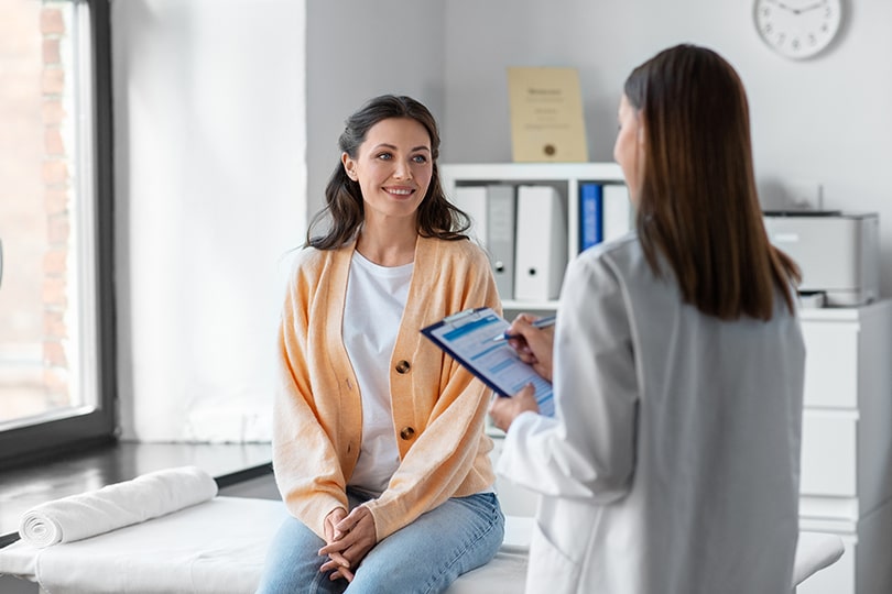 A female patient sitting on the exam table with a female healthcare provider, discussing common questions about menopause.