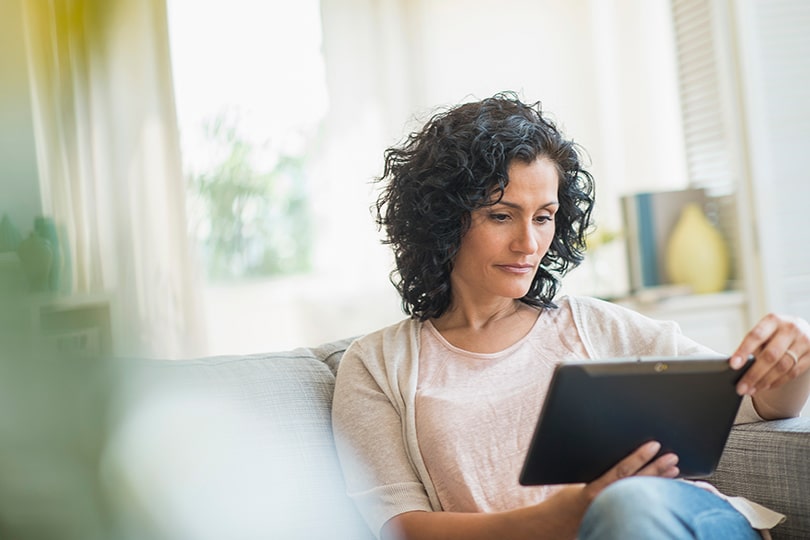 An adult woman sits on a couch looking at a tablet, researching how luteinizing hormone testing can help monitor ovulation and reproductive health.