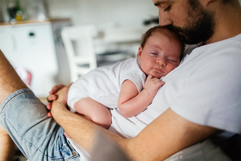 A young adult man holding a baby while thinking about the role of testosterone in fertility and reproductive health. 