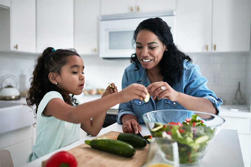 A mom in the kitchen with her young daughter preparing a salad, teaching her about micronutrients and their role in health. 