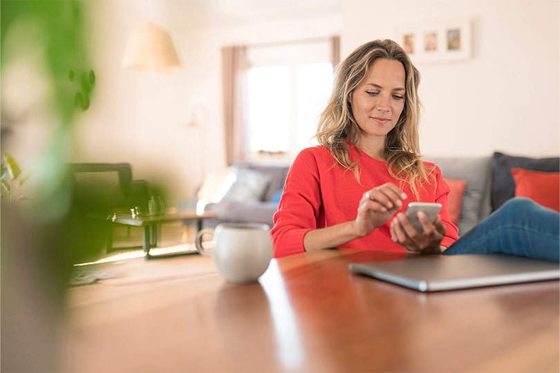 A woman sitting at a table looking at her phone, researching what progesterone levels mean for health and fertility.