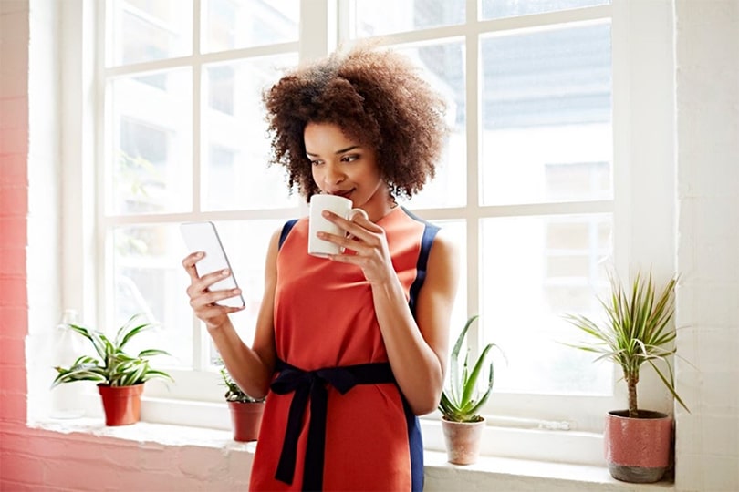 A woman drinking coffee and reading about ApoB and heart health on her phone.