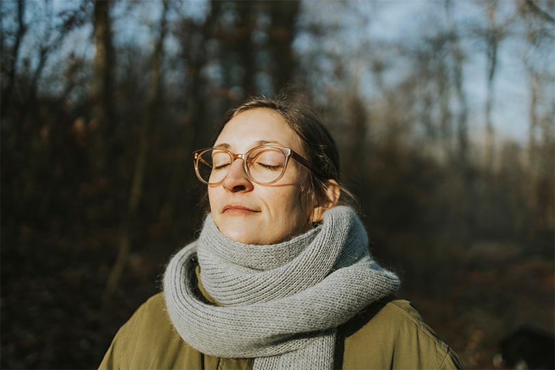 A woman standing outside wearing a scarf, thinking about ways to prioritize her health in the winter 