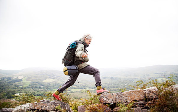 Woman in hiking gear with backpack, smiling while traversing rocky terrain. Foggy atmosphere surrounds the rugged landscape