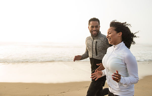 Male and female running on the beach to improve their heart health