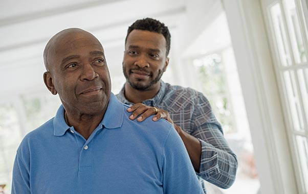 A man offers support by holding an older man's shoulder, highlighting the significance of heart health and ApoB awareness.