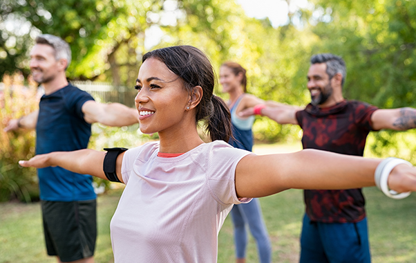 Group of multiethnic mature people stretching arms outdoor. Middle aged yoga class doing breathing exercise at park. Beautiful women and fit men doing breath exercise together with outstretched arms.