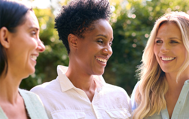 Three women smiling joyfully together outdoors under the warm sunlight.