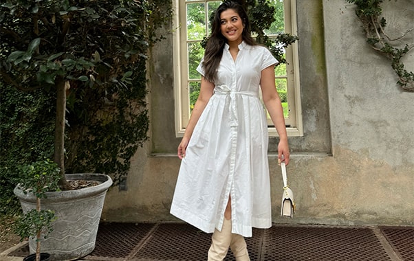 A woman wearing a white dress poses in front of a window, showcasing a stylish and serene atmosphere.