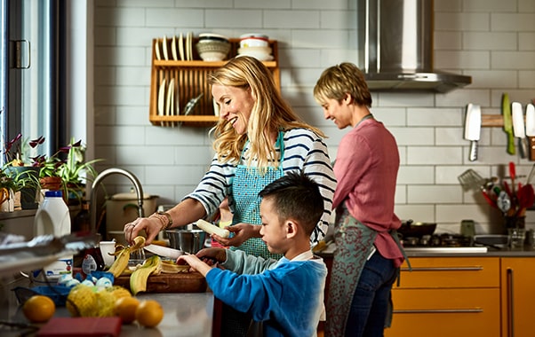 A woman and her two children are seen in the kitchen, actively preparing food, fostering a sense of togetherness and joy