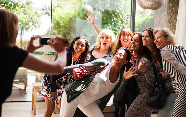 A diverse group of women smiling together while taking a selfie outdoors, capturing a joyful moment of friendship.