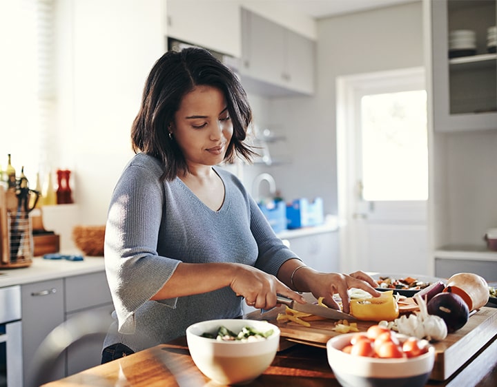 A woman prepares a meal by chopping colorful vegetables on a cutting board in a bright kitchen setting