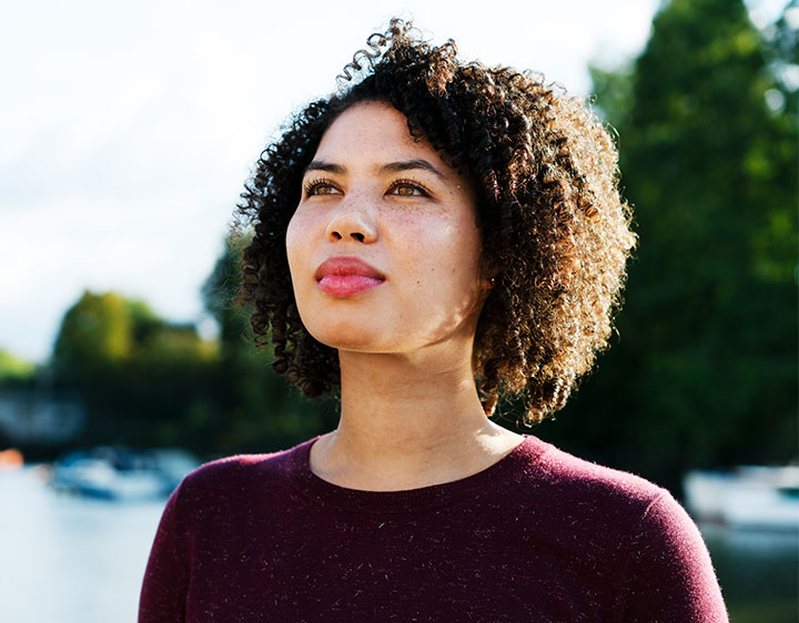 Woman with thoughtful expression standing outdoors, representing consideration of female testosterone testing. 