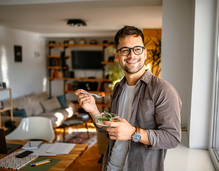  A man in glasses holds a bowl of salad, featuring a mix of fresh greens and colorful vegetables, promoting a nutritious meal