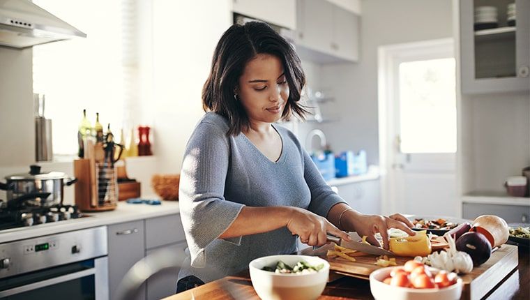 A woman prepares a meal by chopping colorful vegetables