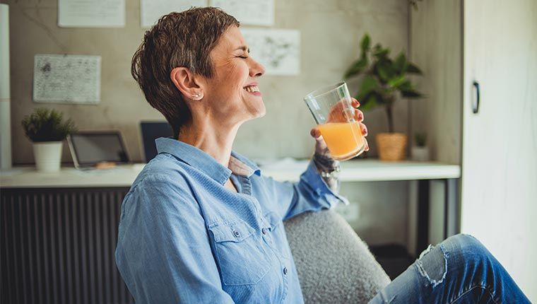 A woman enjoying a refreshing glass of orange juice in her hand.