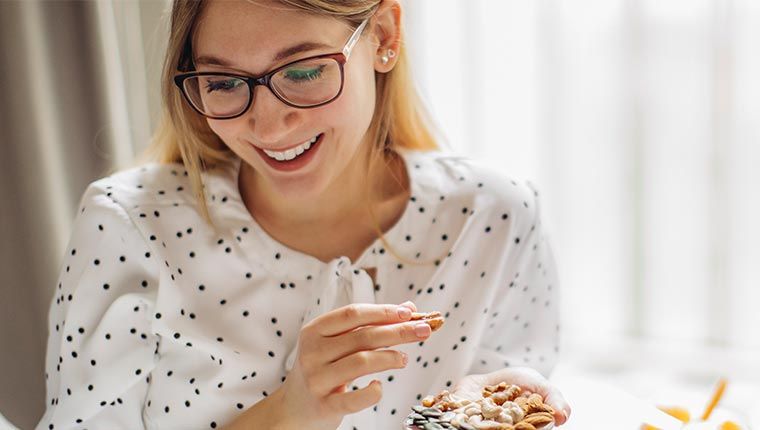 A woman wearing glasses enjoys a variety of nuts and food